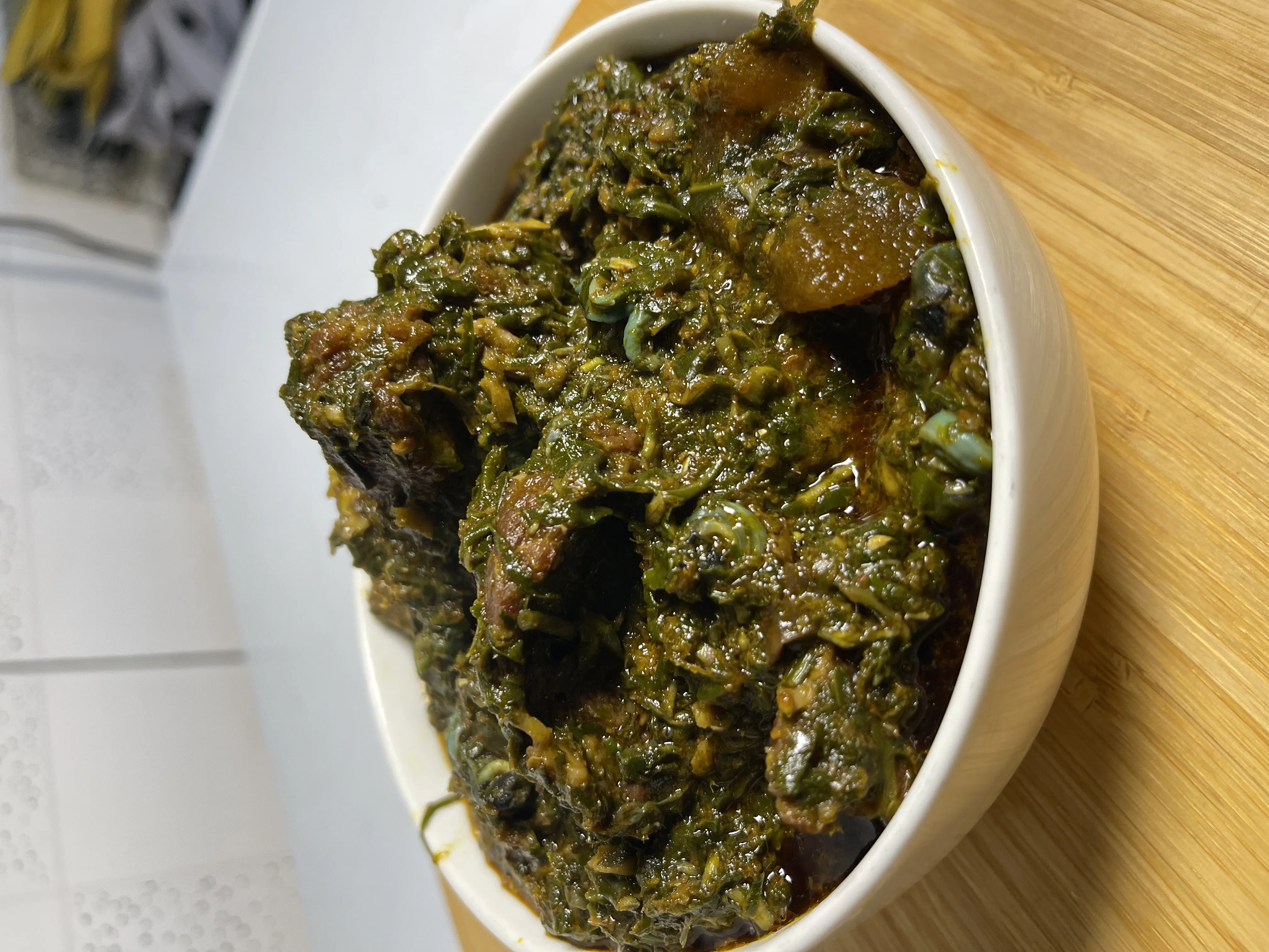 Rich afang soup with dark green leafy vegetables and assorted meat in a white bowl