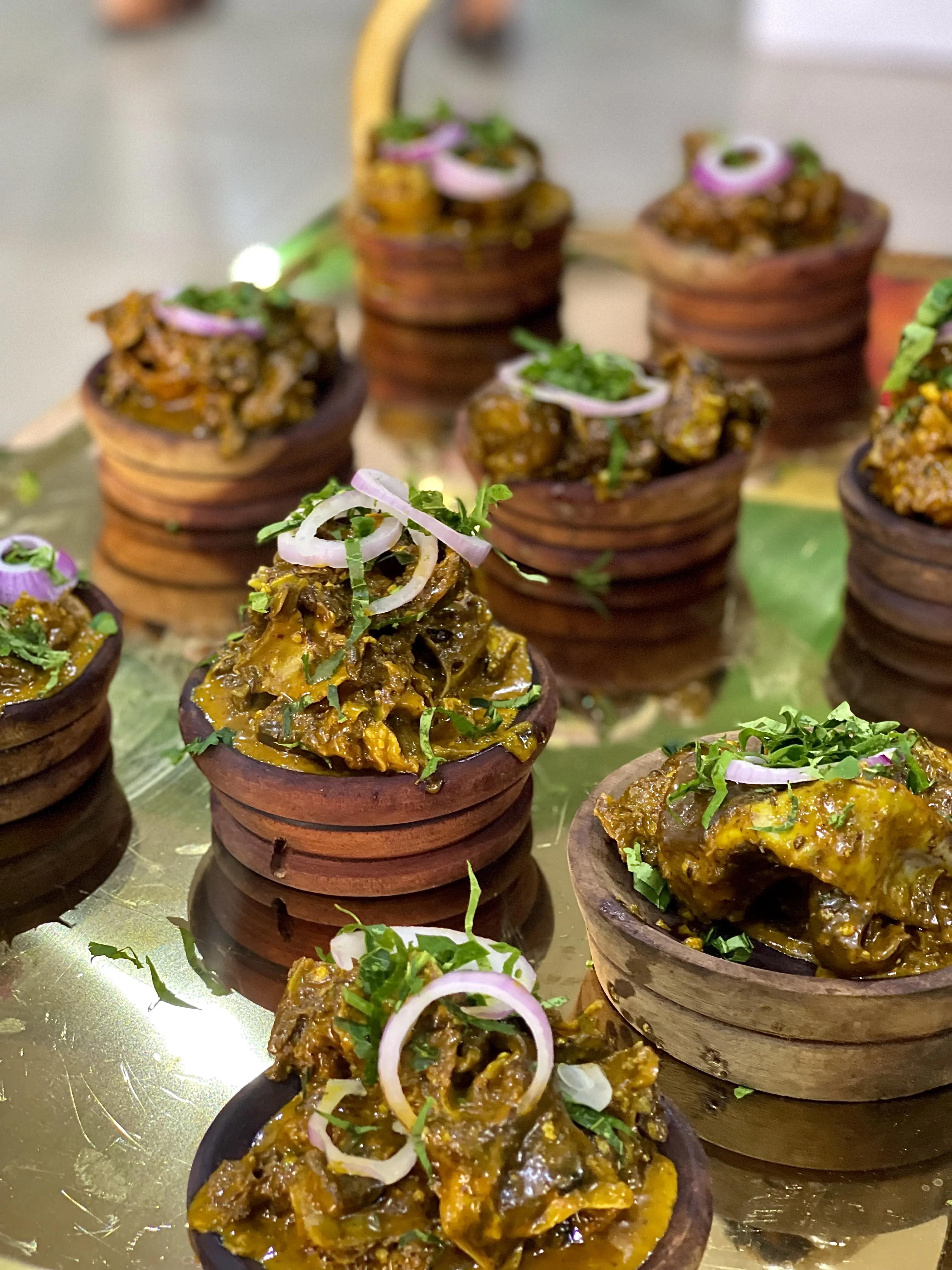 Isi ewu served in traditional wooden pots garnished with fresh onion rings and herbs