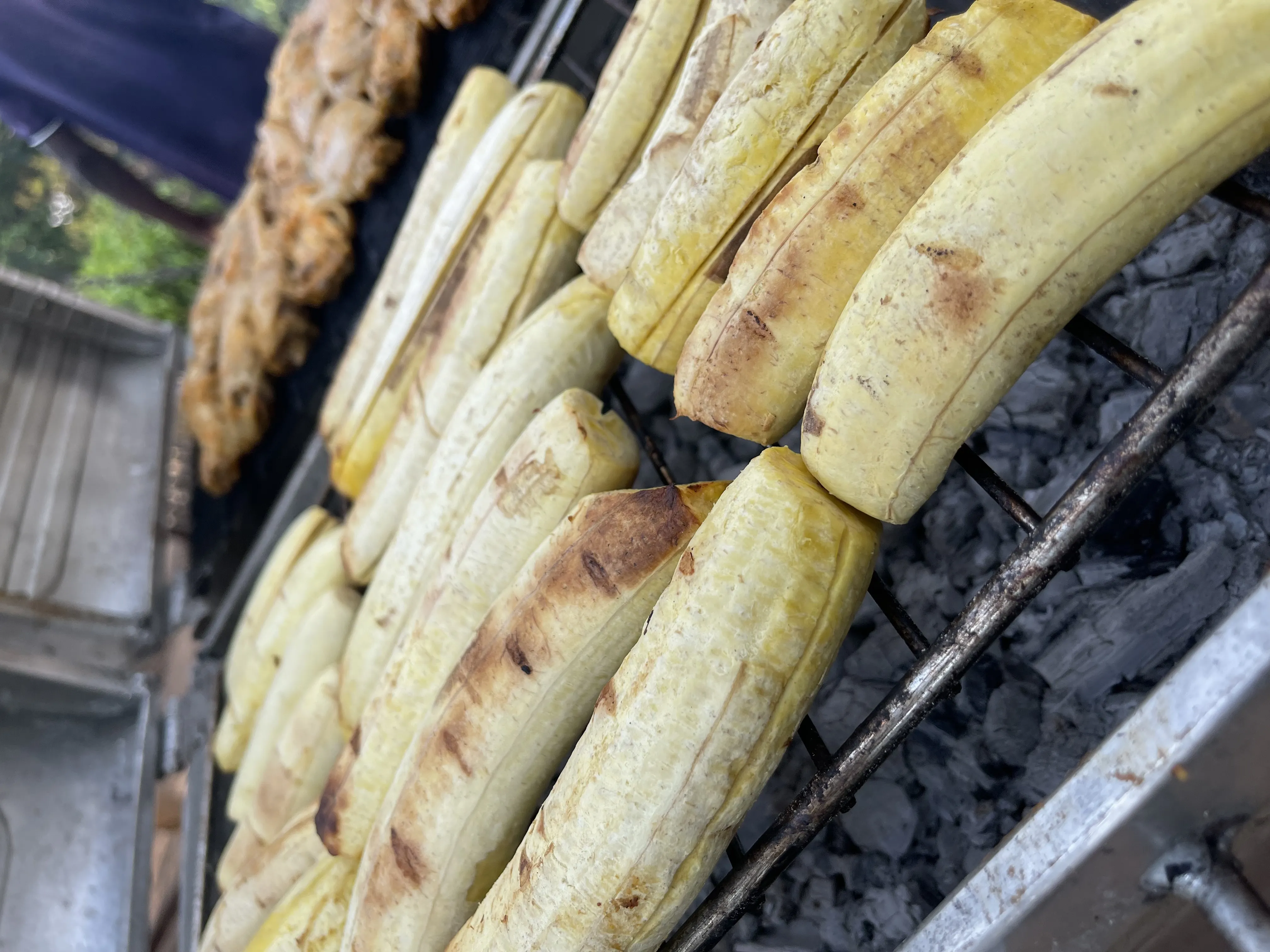 Plantain and chicken grilling on charcoal at an outdoor catering setup